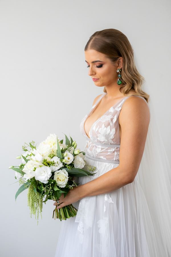 Bride holding elegant white and green bouquet featuring roses, lisianthus and eucalyptus leaves