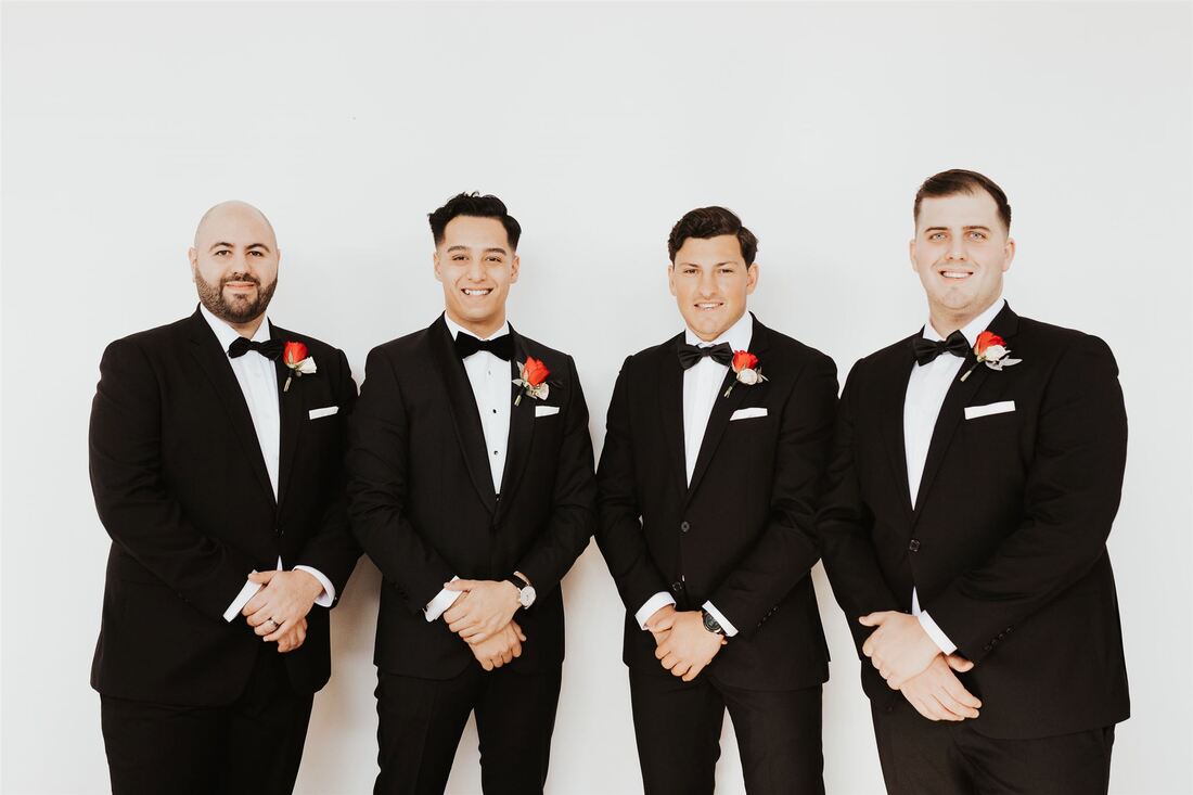 Groom and groomsmen in tuxedos with red rose buttonholes