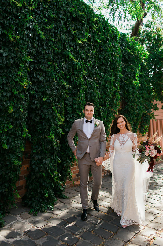 Bride and groom with bride holding a boho bouquet of burgundy, blush and silver flowers. 