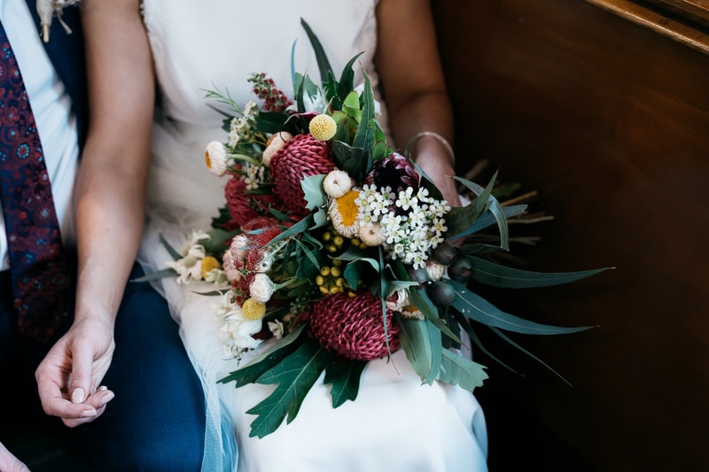 Bridal bouquet of native waratah, proteas, billy buttons, flannel flower and strawflower in pink, red and white with pops of yellow. 