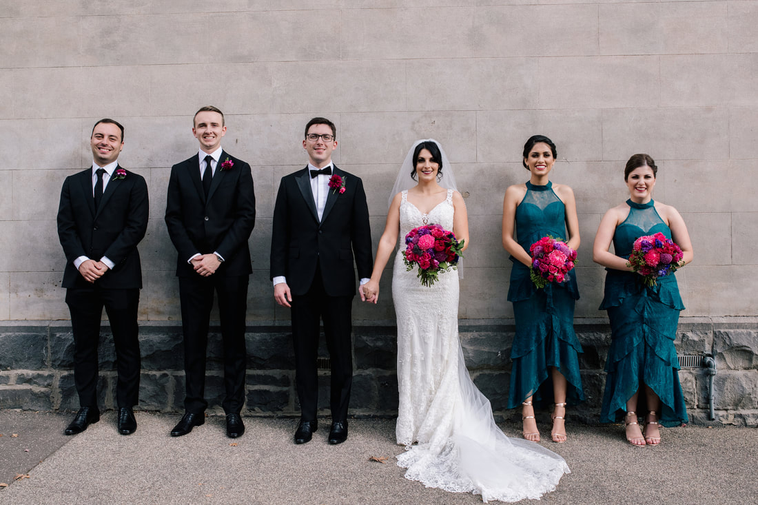 Bridal party with bright jewel toned dresses and flower bouquets of roses and disbuds. 