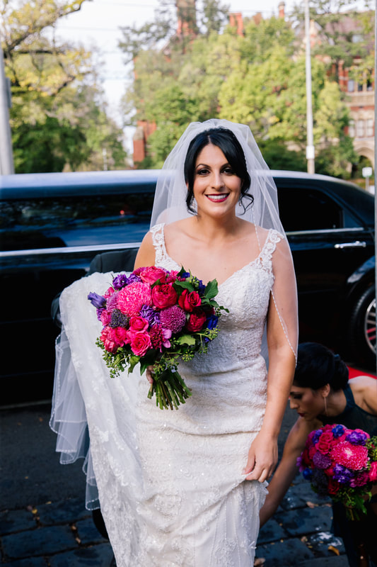 Bride holding bright jewel toned wedding bouquet and getting out of wedding car. 