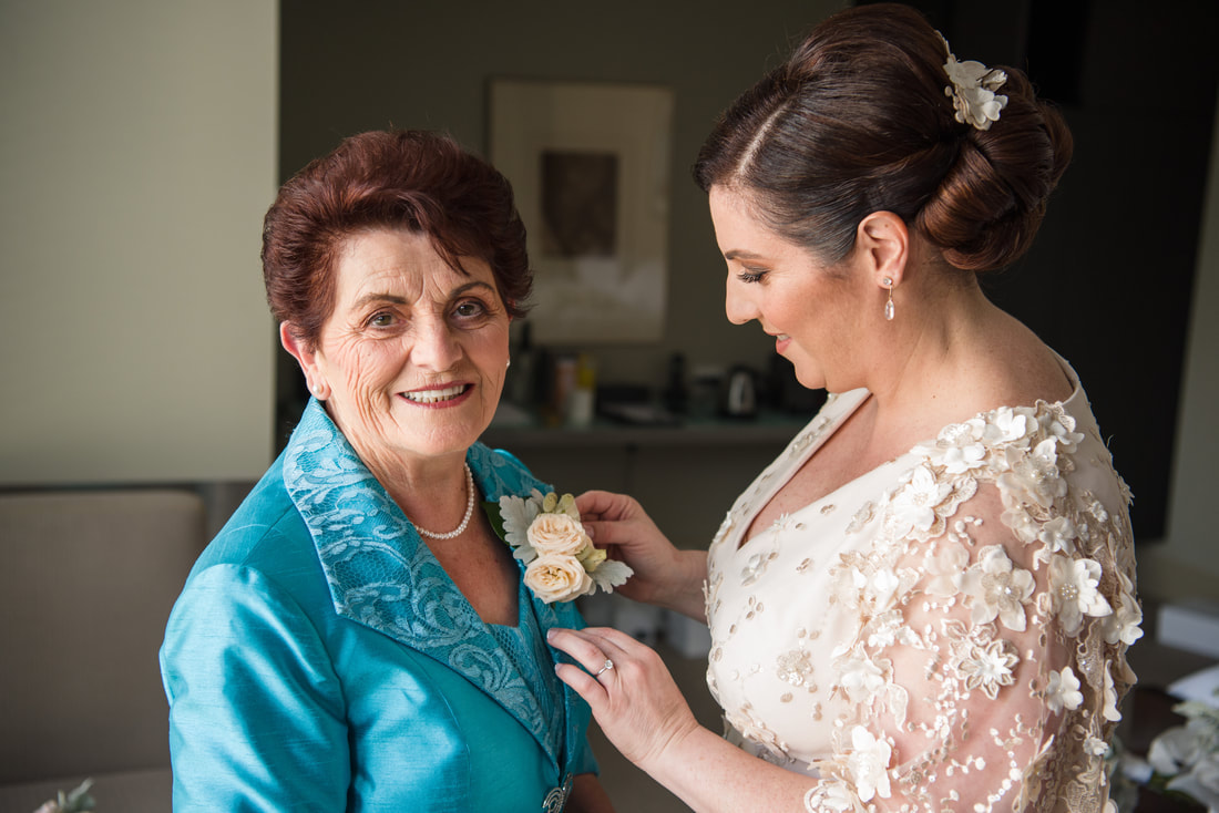 Bride pins pastel flower corsage onto her mother on wedding morning. 