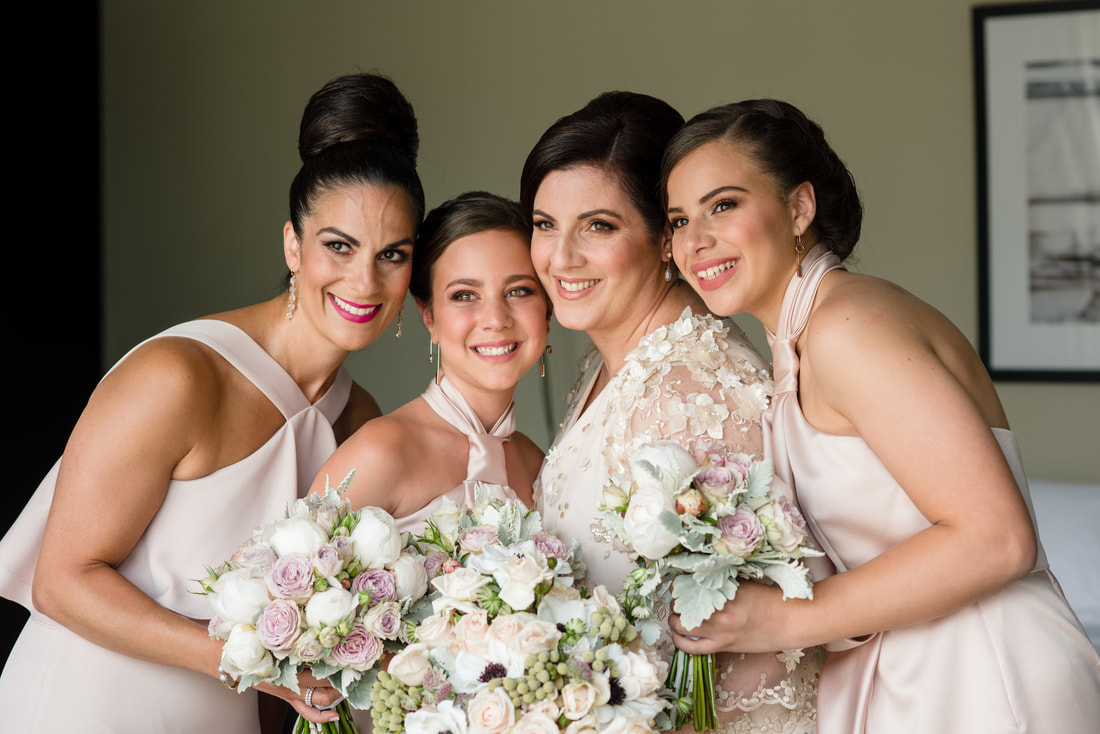 Bride and her bridesmaids hold bouquets of soft pink and white flowers including roses and anenomes