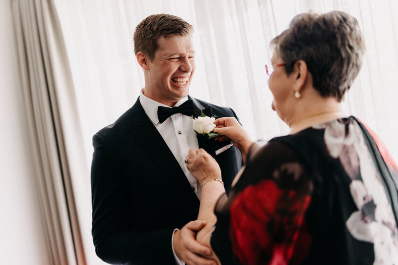 Mother pins white rose buttonhole on groom wearing black tuxedo