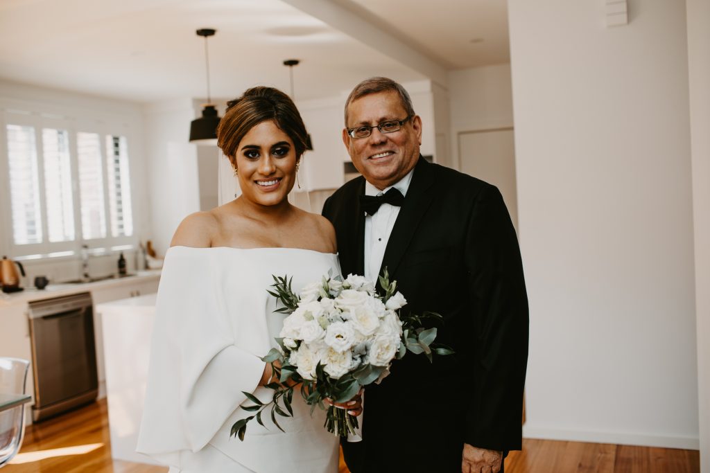 Bride and her father on wedding day holding bouquet of white roses and green foliage
