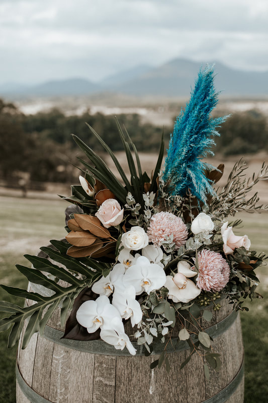 Wine barrel arrangement at Riverstone Estate with pampas grass, roses and orchids in sage and cinnamon tones with pops of teal. 