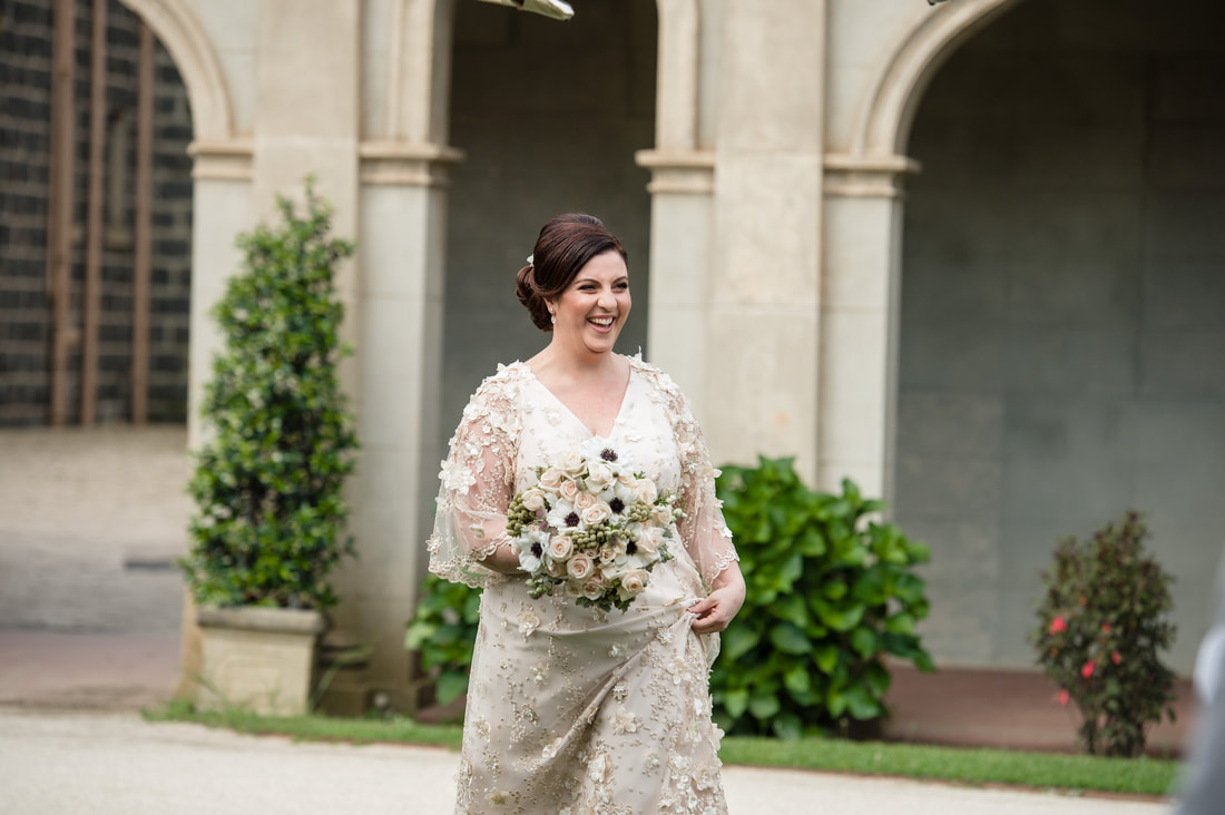 Bride walks down the aisle to her groom at Werribee Park Mansion holding a bouquet of white and pink roses and anenomes. 
