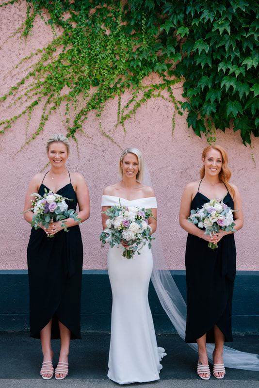 Bride and her bridesmaids holding pastel flower bouquets of roses, dahlias and eucalyptus in silver, white and lilac tones