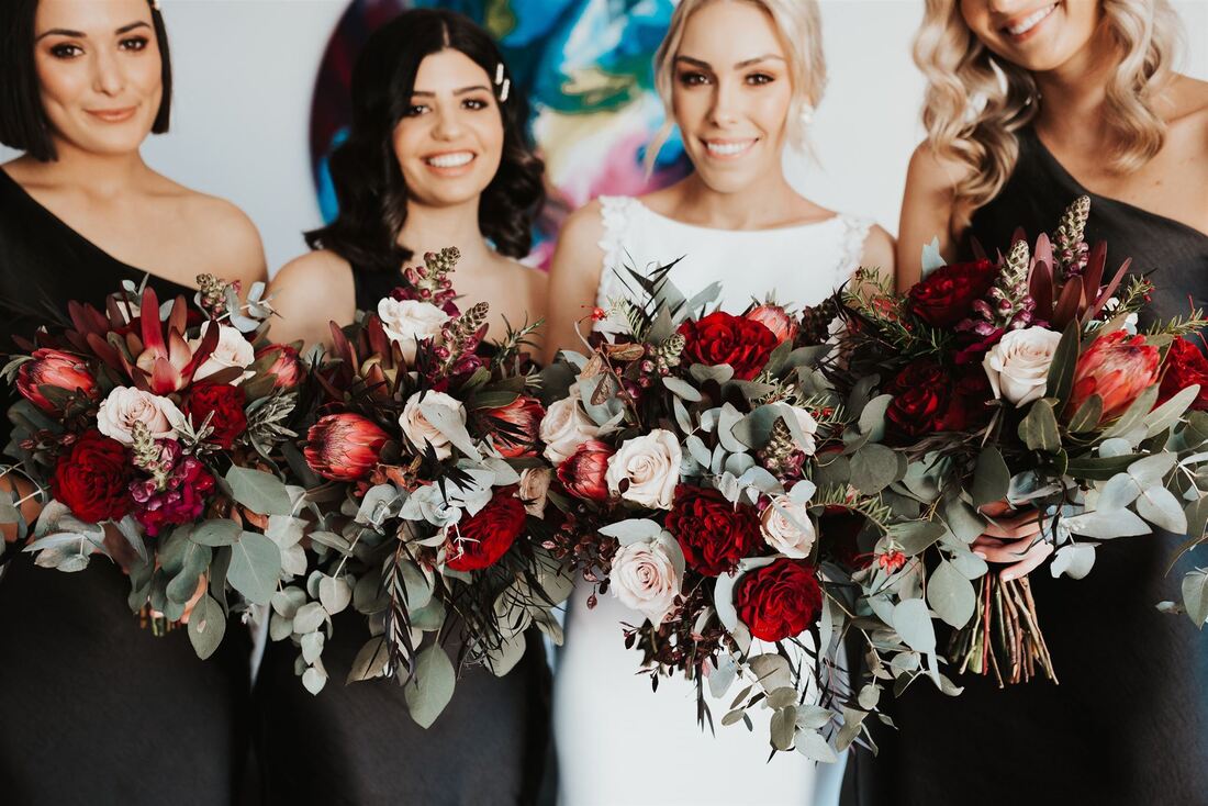 Bride and bridesmaids holding natural wedding bouquets with burgundy roses