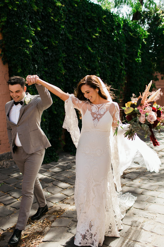 Bride and groom with bride holding a boho bouquet of burgundy, blush and silver flowers. 