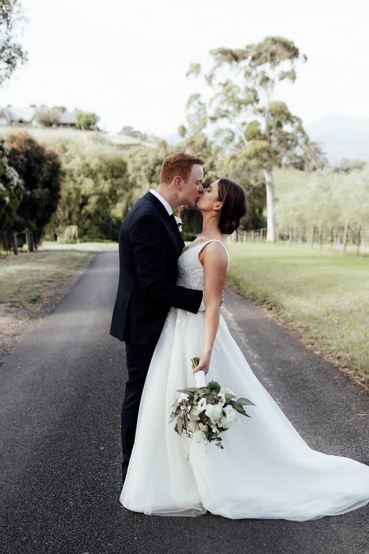 Bride and groom share a kiss at the Riverstone Estate, Yarra Valley. Bride holds a bouquet of white and green flowers. 