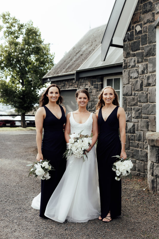Bride and her bridesmaids holding white and green flower bouquets. Bridesmaids wearing elegant black dresses. 