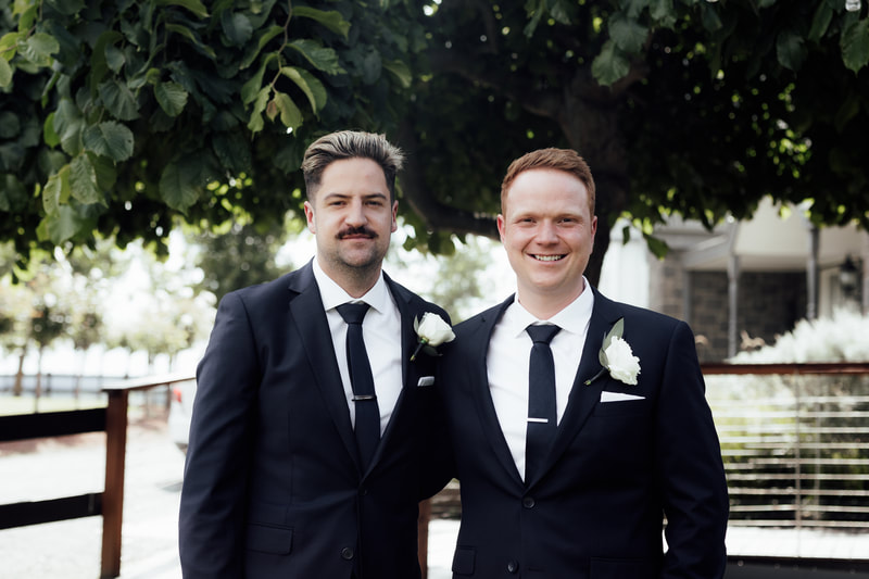 Groom and groomsmen wearing black suits with white rose buttonholes. 
