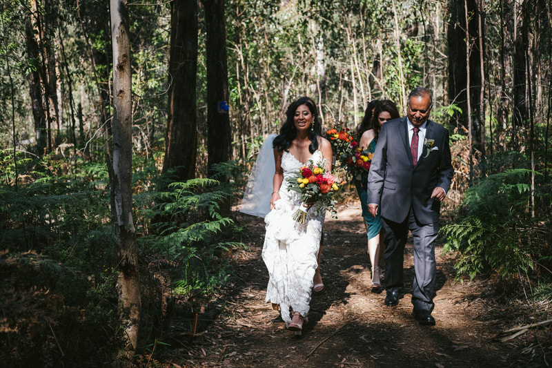 Bride walks down the forest aisle carrying a bouquet of bright native flowers at Forest Weddings Kinglake