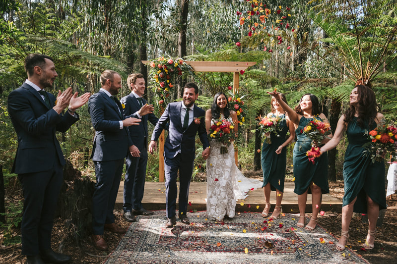 Bride and groom walk down the aisle as guest throw bright rose petal confetti 