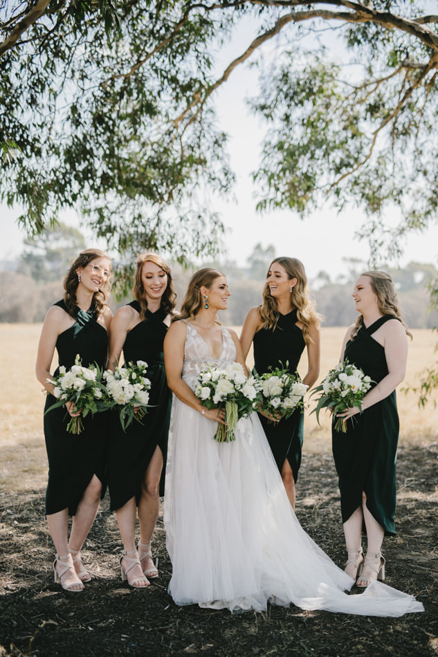 Bride and her bridesmaids holding rustic white and green flower bouquets featuring roses, dahlias and amaranthus. 