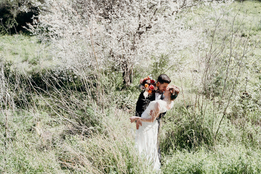 Bride and groom in meadow with rustic bouquet. 