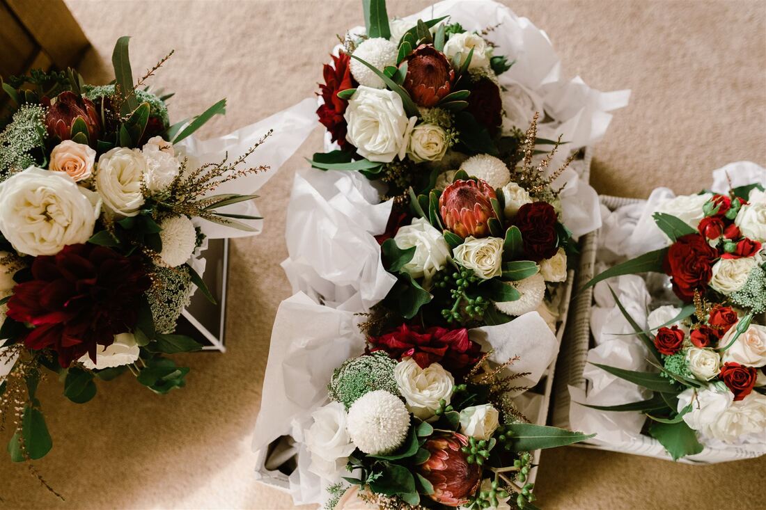 Wedding bouquets of proteas, roses, dahlias and queen anne lace in red, burgundy and white. 