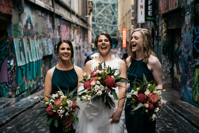 Bride and her bridesmaids in Melbourne's graffiti laneways holding native flower bouquets. 