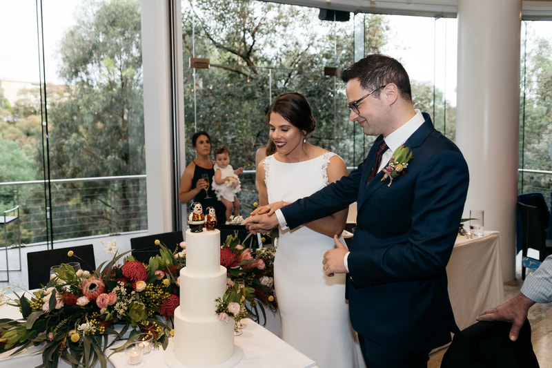Bride and groom cut the cake on their wedding day. Cake is decorated with native flowers and Babushka dolls. 