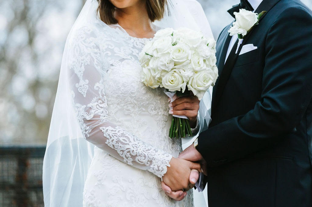 Bride holding traditional bouquet of white roses.