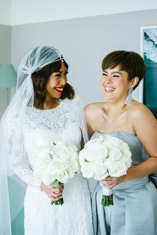 Elegant bride and bridesmaid holding traditional white rose wedding bouquets. 