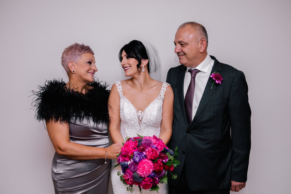 Bride and her parents with bride holding bright jewel toned wedding bouquet. 