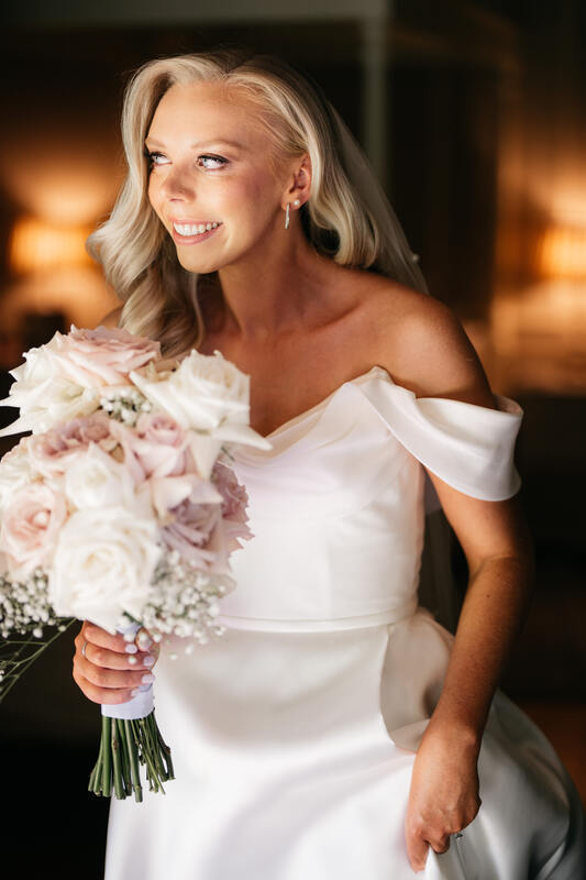 Bride holds a bouquet of reflexed white and blush roses with babies breath and orchid. 