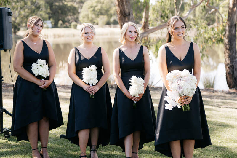 Bridesmaids in black dresses holding white reflexed rose bouquets. 