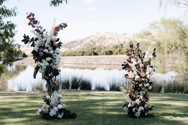 Wedding ceremony column arbour, asymetrical in style at Flowerdale Estate. Blush, white and toffee flowers with dark foliage. 