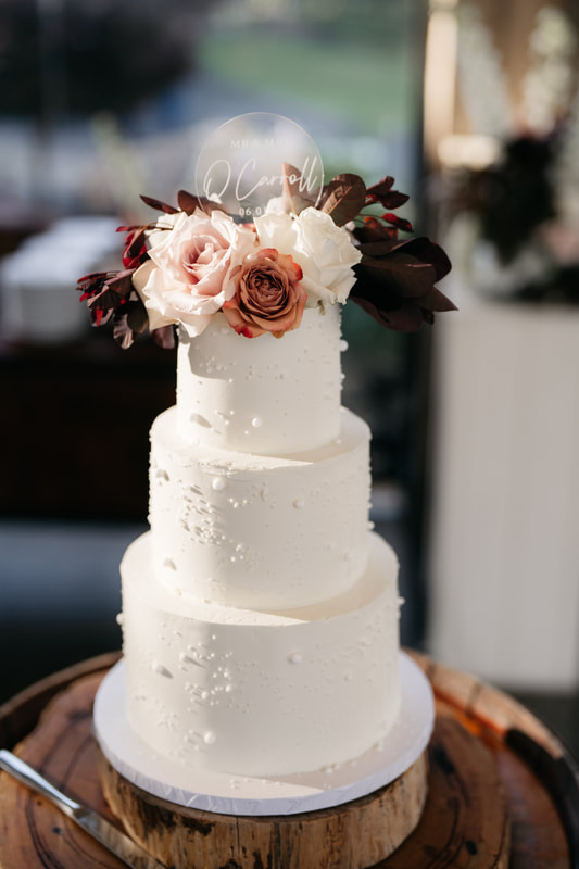 White buttercream wedding cake decorated with pink and toffee flowers. 