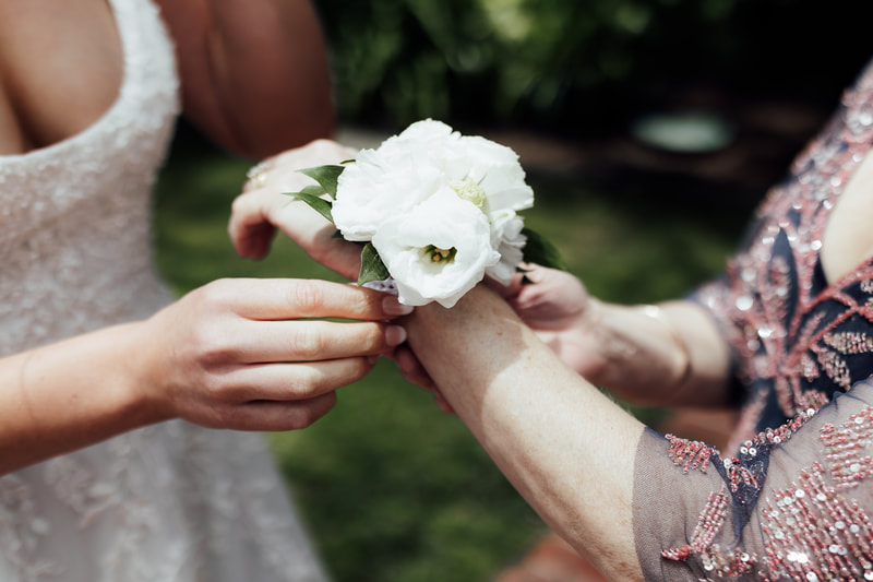 Elegant white wrist corsage being placed on the wrist of mother of the bride. 