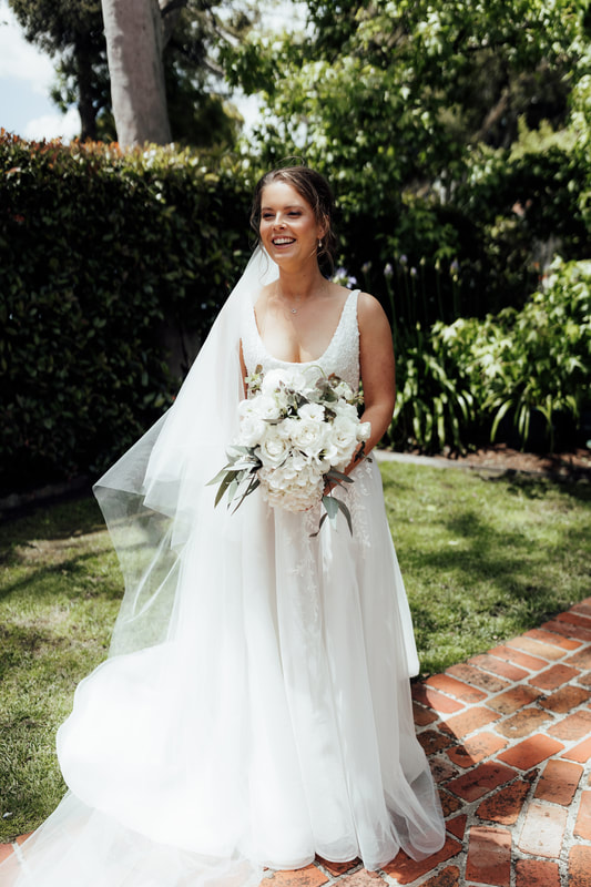 Bride holding a bouquet of white flowers including roses and hydrangea. 