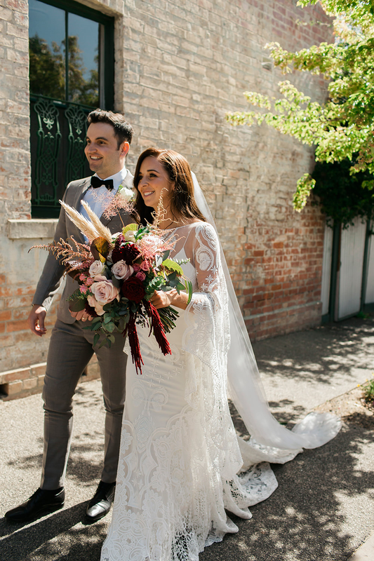Bride carrying large bouquet of flowers in a boho style with pampas grass, amaranthus, roses and astillbe in red and pink tones. 